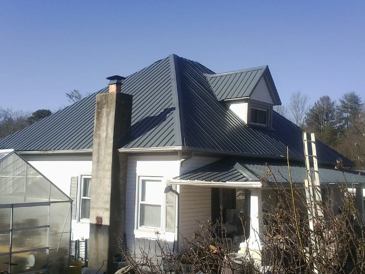 Dark blue standing seam metal roof on a white farmhouse with dormer — Slate & Tile Roof Repair by Roofing Brothers in Winton