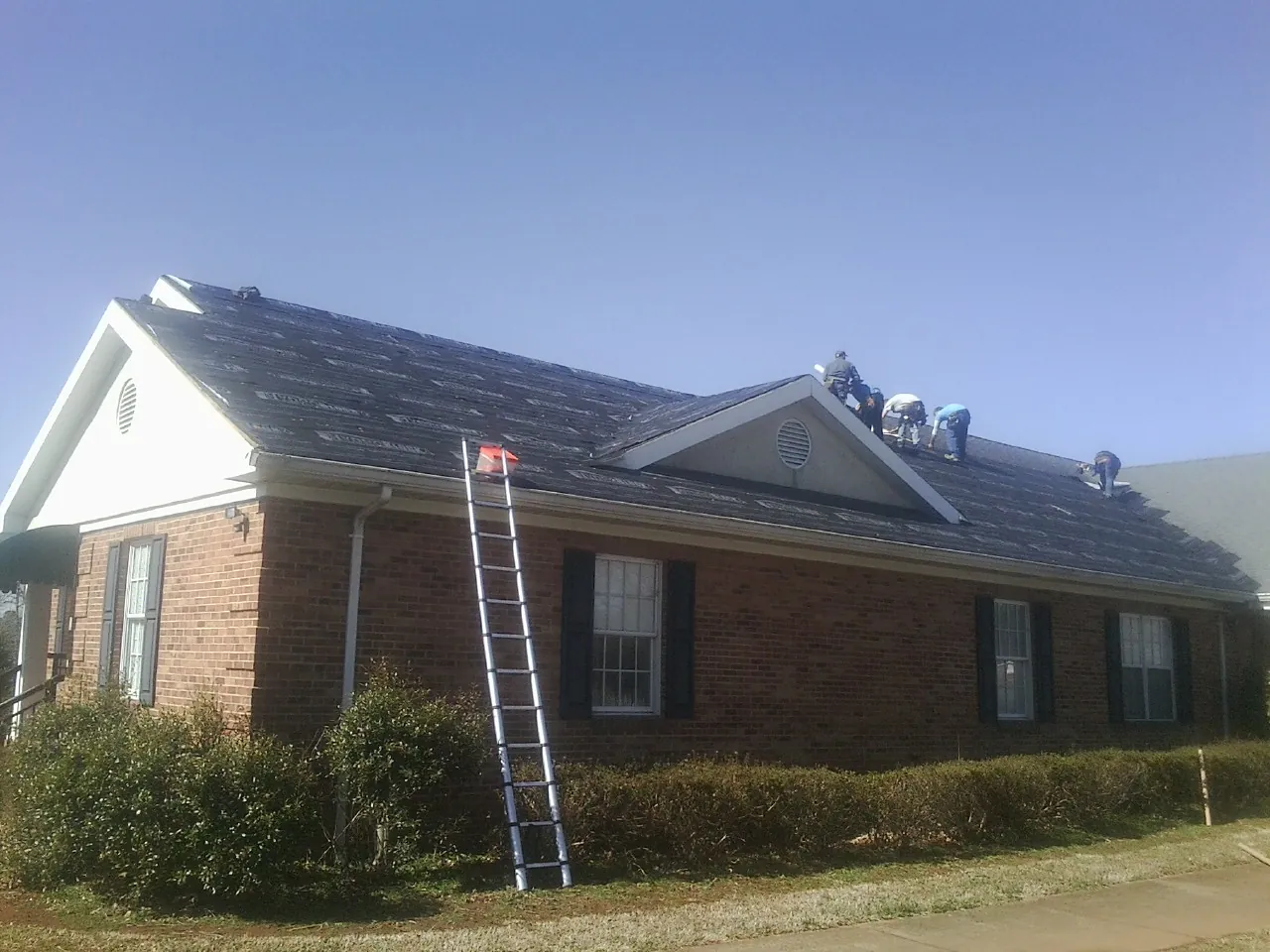 Crew tearing shingles off a brick ranch roof with a ladder set — Emergency Roof Repair work by our crew in Winton