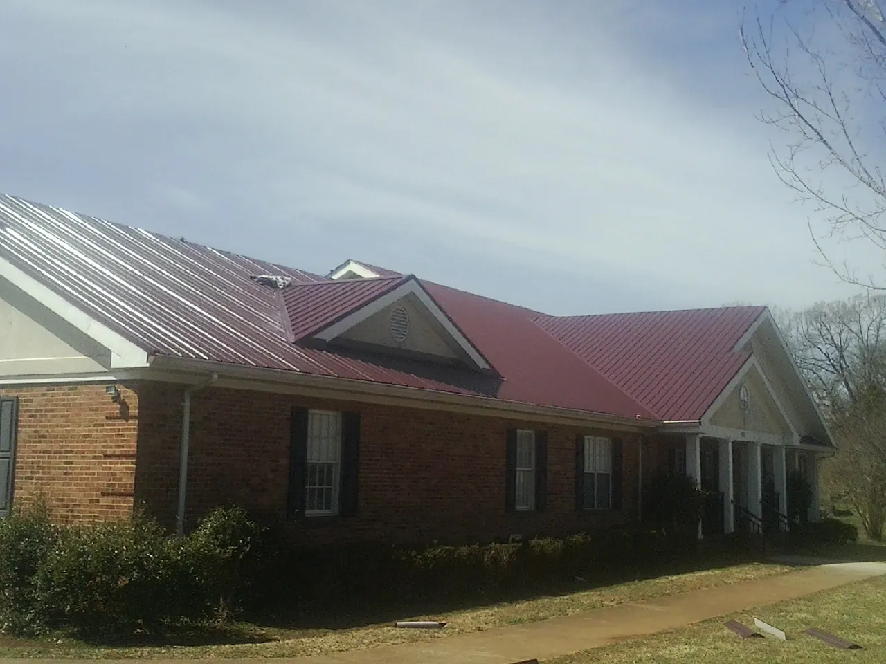 Red metal roof with gabled entries on a long brick building, from a Hail Damage Roof Repair job in Winton