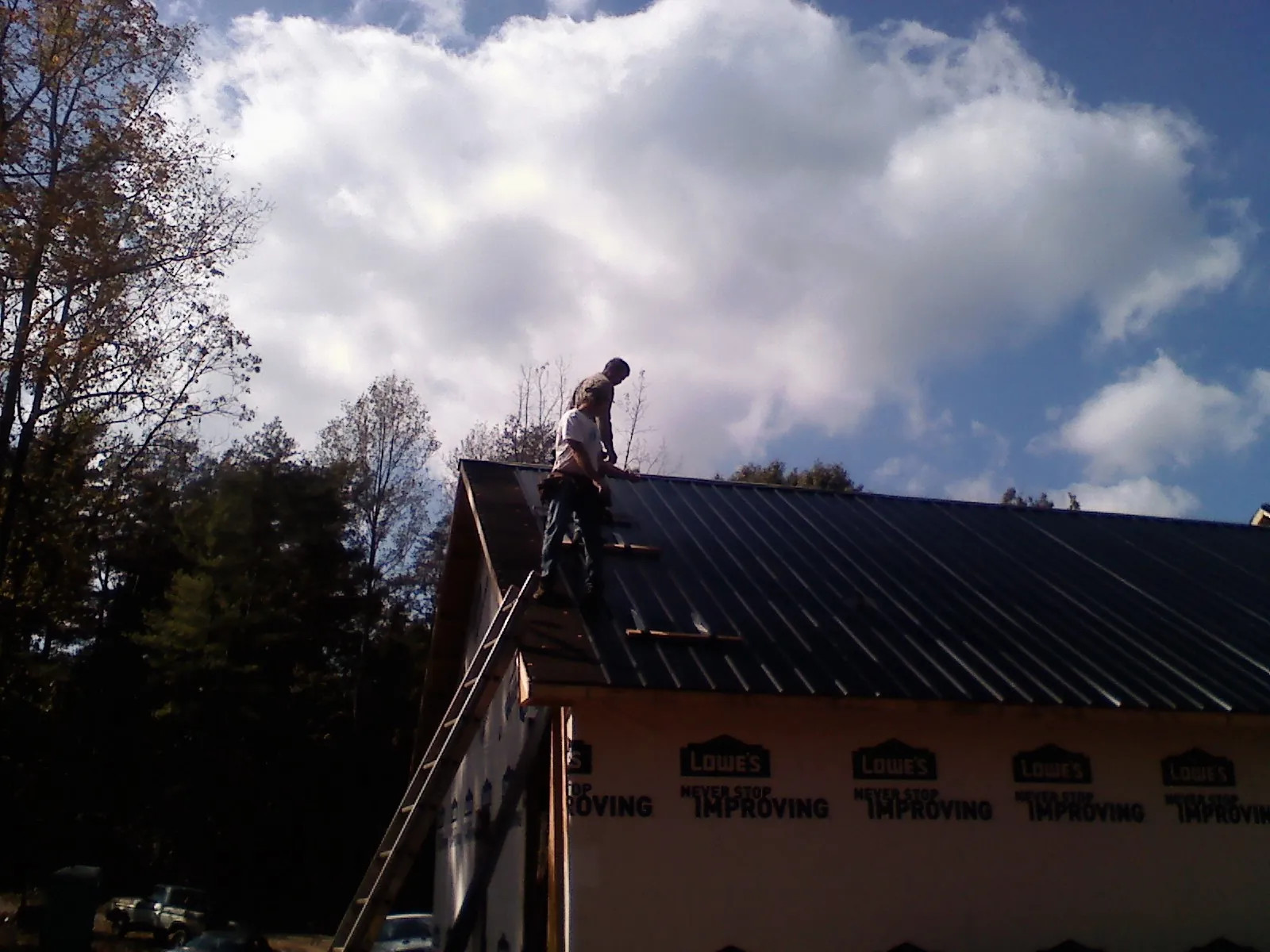 Roofer fastening dark metal panels high against a cloudy sky, from a Roof Inspection job in Winton