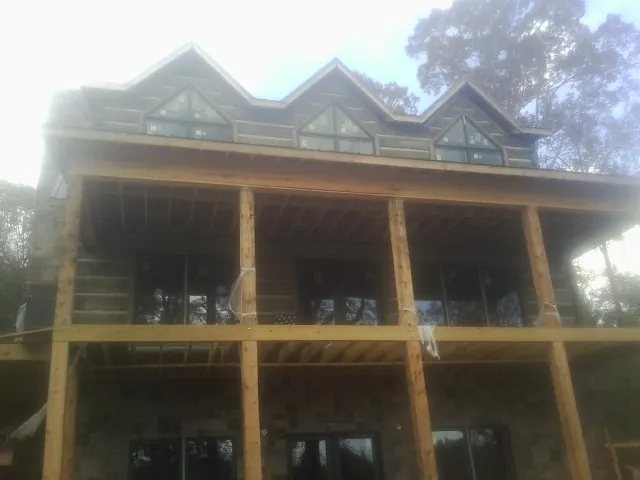 Dormers and porch framing on a large log home under construction — Roof Coating work by our crew in Winton