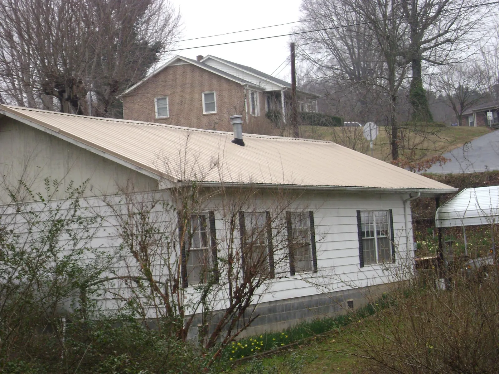 Tan metal roof on a white sided house set into a hillside — Commercial Roofing by Roofing Brothers in Winton