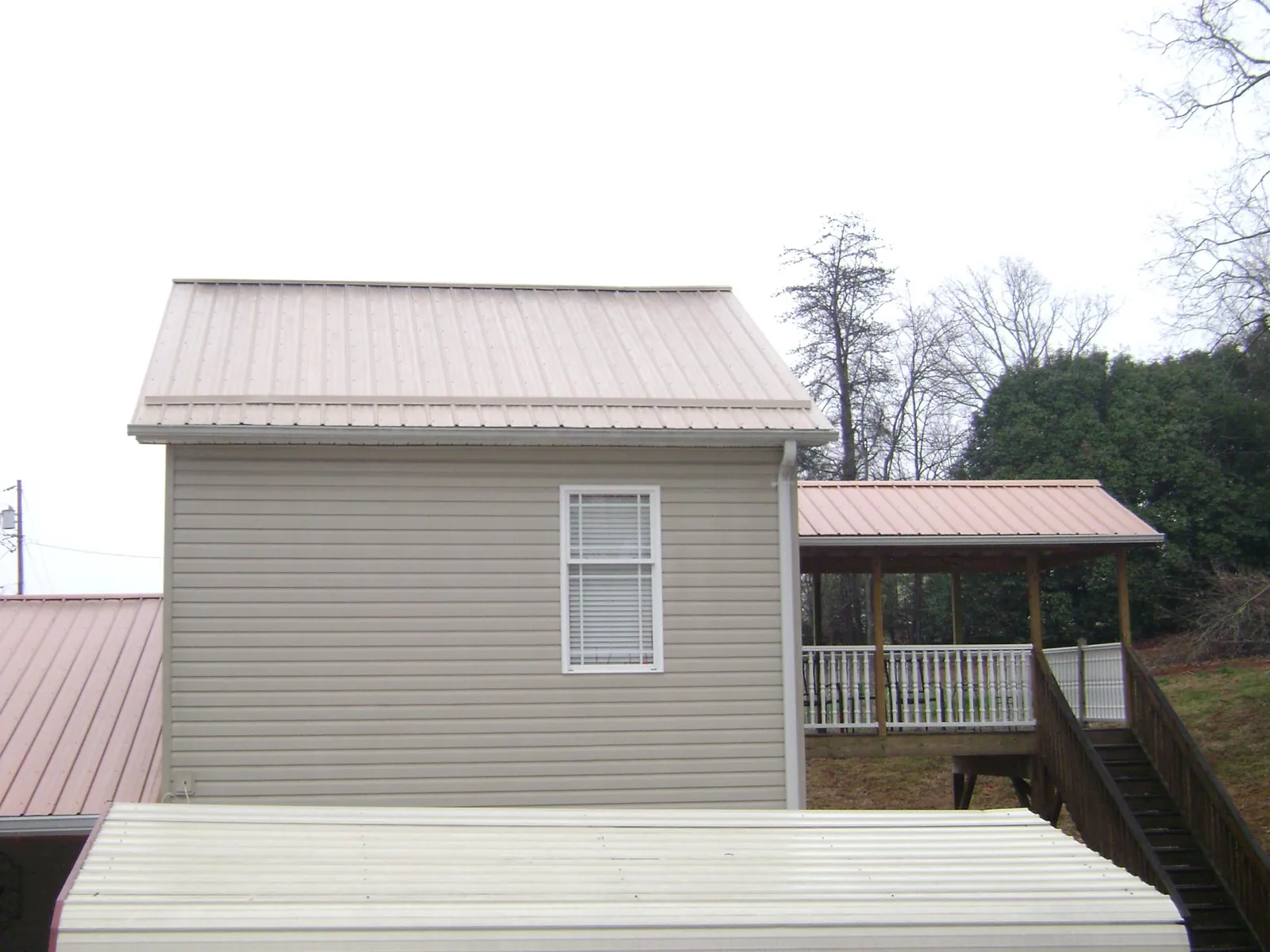 Tan metal roofs on a two story addition and attached porch, from a Roof Replacement job in Winton